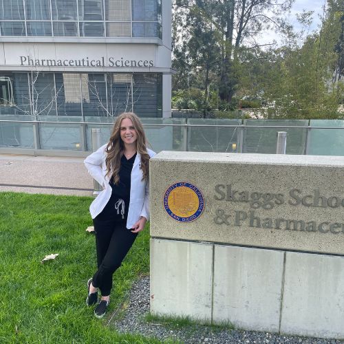 "Pharmacy student leans against a sign that says Skaggs School of Pharmacy"